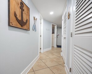 A hallway with a wooden anchor decoration, a sign reading "BEACH HOUSE," and a door with a louvered design.