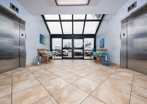 A spacious elevator area with two elevators, a bench, and a blue suitcase.