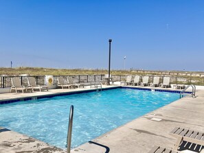 A clear blue swimming pool with a metal ladder, surrounded by lounge chairs and a wooden deck.