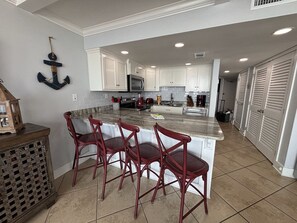 A modern kitchen with white cabinets, a central island with bar stools, and a hanging anchor decoration.