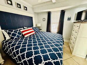 A bedroom with a bed, a dresser, a television, and a window with curtains.
