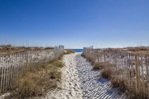 A sandy beach path flanked by wooden fences leading to the sea under a clear sky.