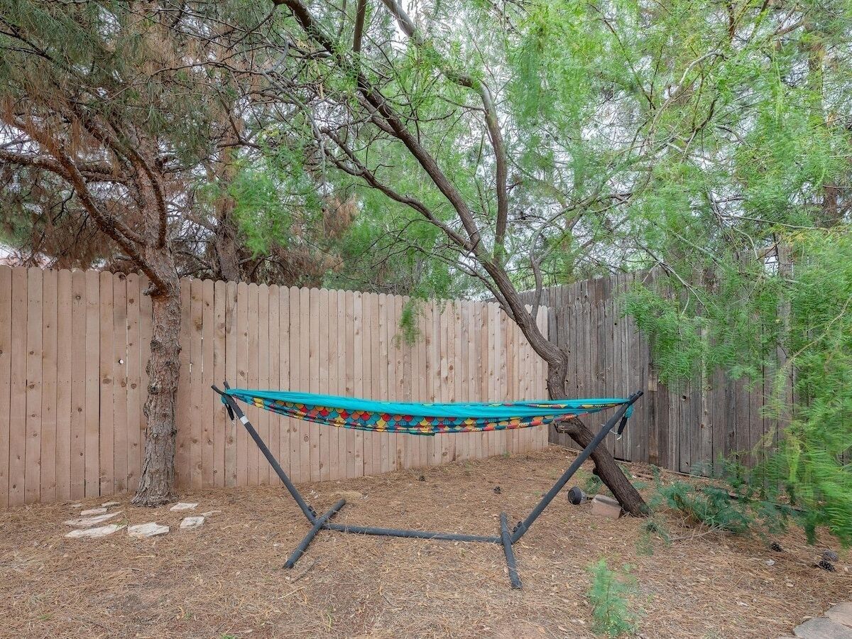 A hammock tied between two trees in a backyard with a wooden fence in the background.