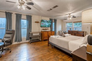 A bedroom with a bed, a chair, a TV, and a ceiling fan. - Midland Manor - Two Homes w/Separate Large Yard+Game Room by LCH (Midland)