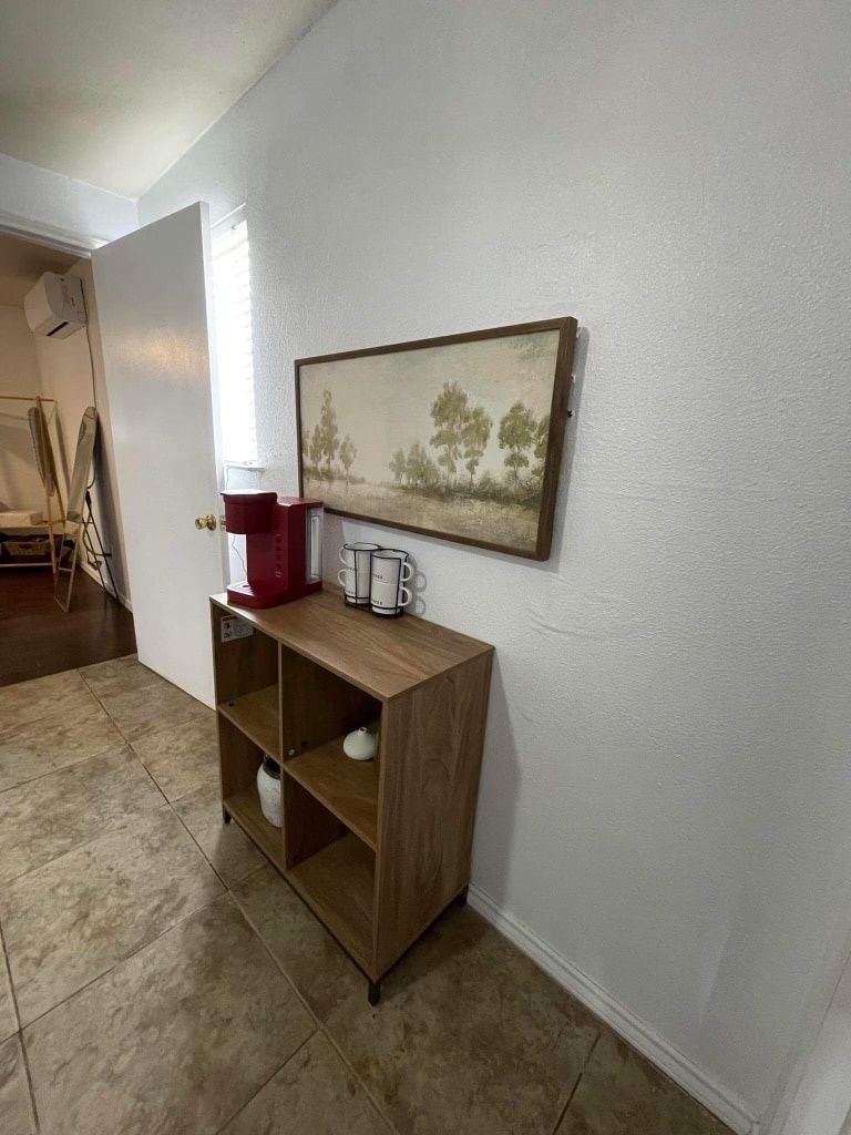A hallway with a wooden console table, a painting of trees, and a door leading to another room.