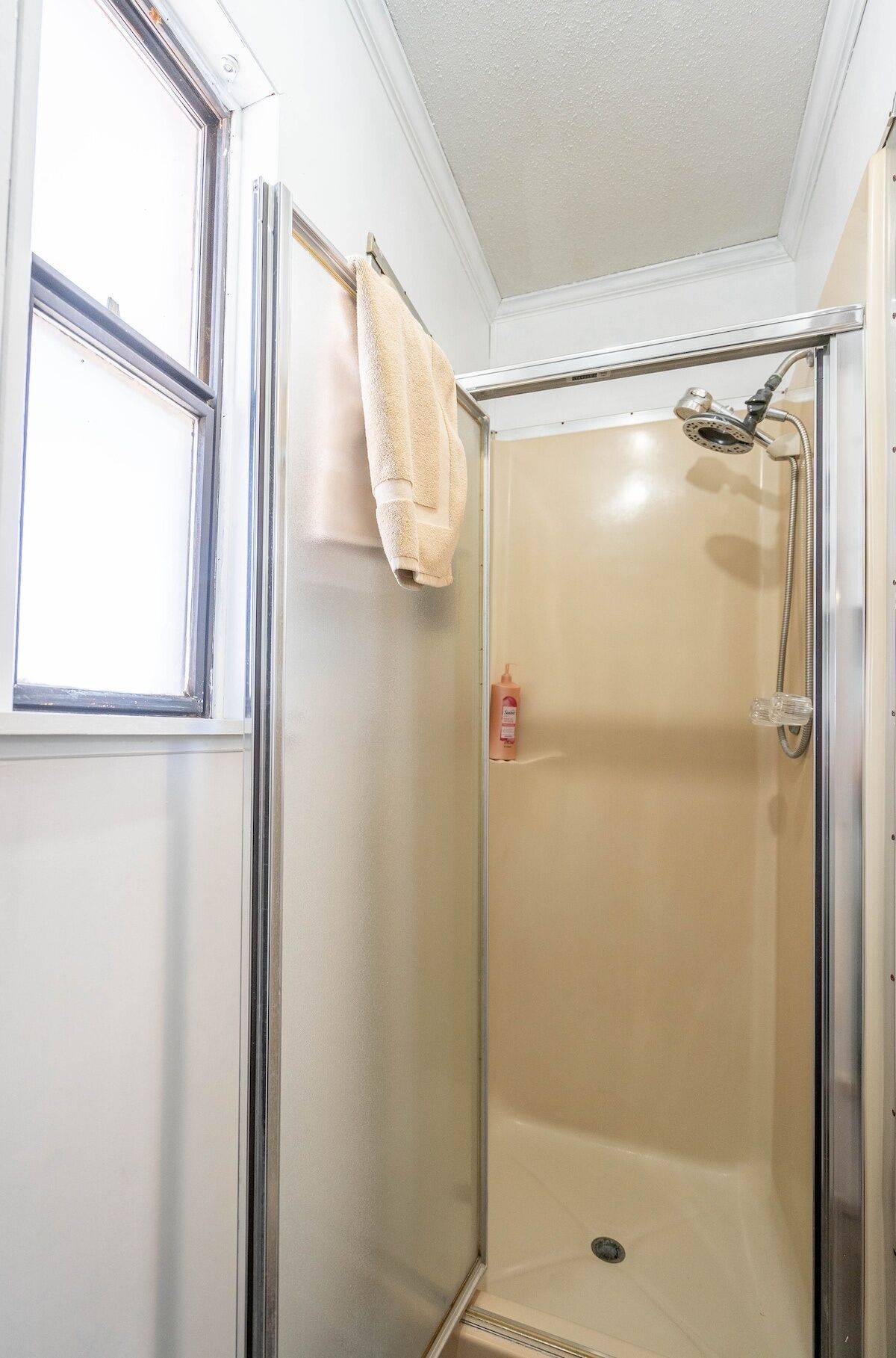 A small, enclosed shower area with a glass door, a towel hanging on the door, and a bottle of shampoo on the floor.