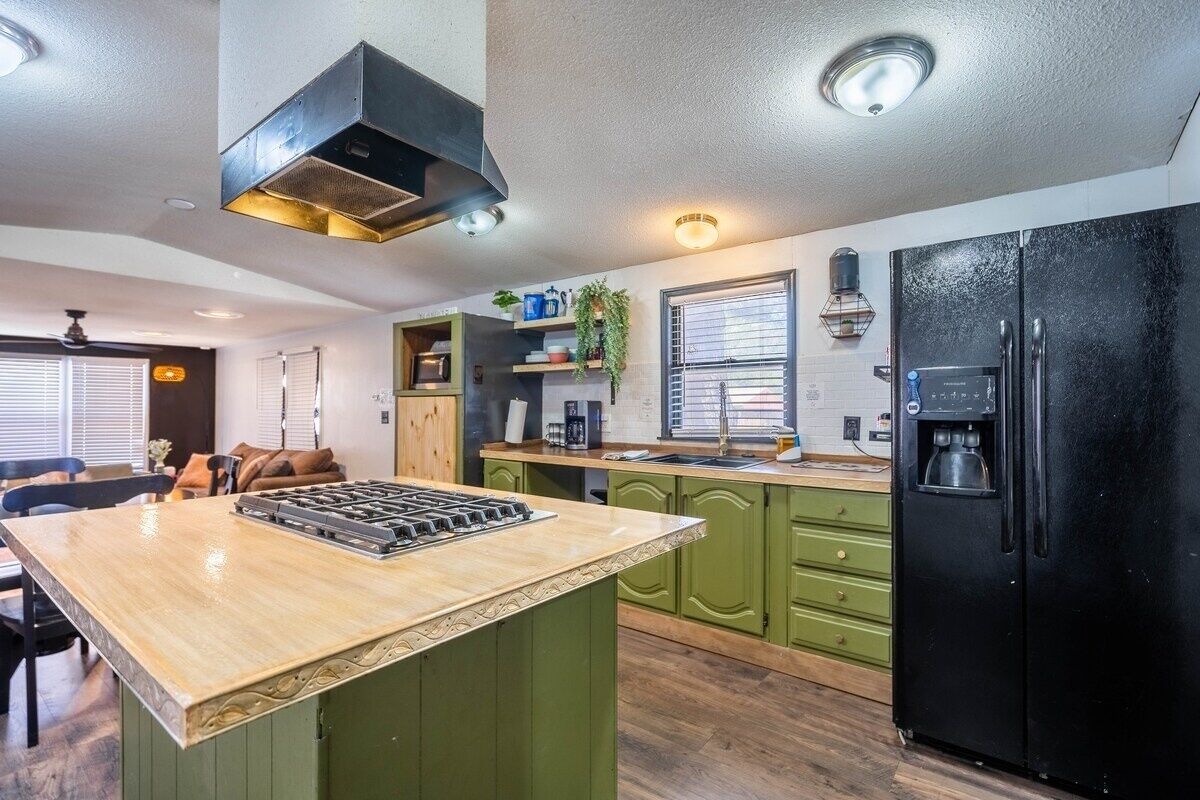 A modern kitchen with green cabinets, a black refrigerator, and a wooden island.