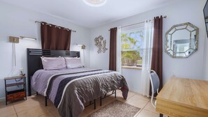 Une chambre à coucher avec un lit, une table de chevet, une lampe, une fenêtre avec des rideaux et un miroir au mur.