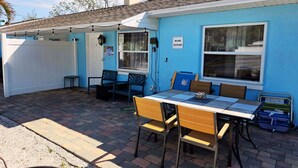 Un espace patio avec une table et des chaises, une clôture blanche et un bâtiment bleu doté d’une fenêtre.