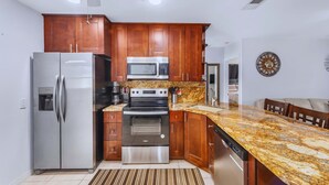 Une cuisine dotée de meubles en bois, d’appareils électroménagers en acier inoxydable, d’un plan de travail en granit et d’un ventilateur de plafond.