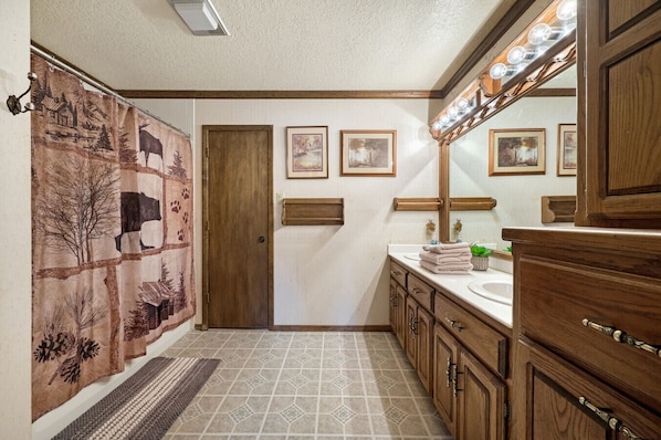 A bathroom with a wooden vanity, a large mirror, and a shower curtain with a nature scene.