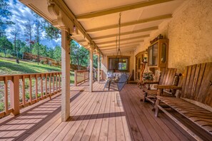 A wooden deck with a hanging chair and a table, a wooden chair, and a wooden cabinet.