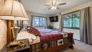 Ein Schlafzimmer mit einem Bett, einem Deckenventilator, einem Fernseher und Fenstern mit Vorhängen.