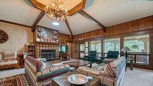 Ein gemütliches Wohnzimmer mit Kamin, Ledersesseln und einem großen Fenster mit Blick auf einen Wald.
