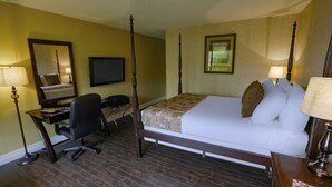 A hotel room with a four-poster bed, a desk with a chair, a television, and two lamps.