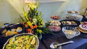 A buffet table with various food items, including salads, pastries, and a floral centerpiece.