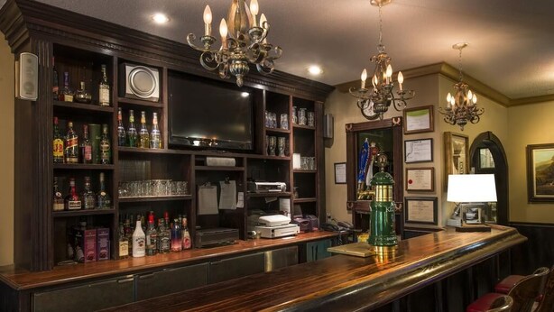 A bar area with wooden shelves stocked with bottles, a television, and a bar counter with stools.
