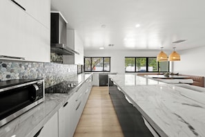 Uma cozinha moderna com bancada de mármore, micro-ondas embutido e painel de pedra atrás do fogão.