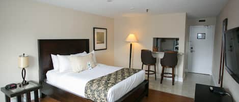 Une chambre d’hôtel comprenant un lit, une table de chevet, une lampe, un bureau, des chaises et un téléviseur.