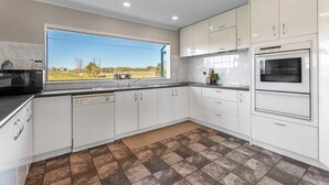 A modern kitchen with white cabinets, a built-in oven, a dishwasher, and a large window offering a view of the outdoors. - ⭐The Pond House by Homello⭐ | Pool • Pond • Peaceful Country Retreat (Karaka)