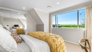 A bedroom with a large bed, a mirror, and a view of green fields. - ⭐The Pond House by Homello⭐ | Pool • Pond • Peaceful Country Retreat (Karaka)