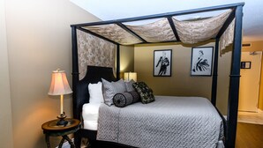 Ein Himmelbett mit einer gesteppten Tagesdecke, zwei Nachttischlampen und einem kleinen runden Tisch mit einer Lampe.