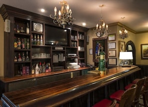 Zona de bar con estantes de madera llenos de botellas, un televisor y una barra con taburetes.