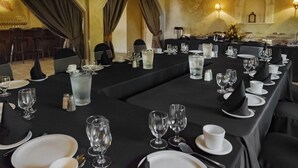 A formal dining room with long tables set for a meal, featuring clear glassware and white plates.