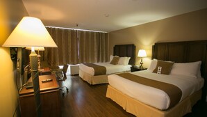 A hotel room with two beds, a desk, and a chair. There are lamps on either side of the room.