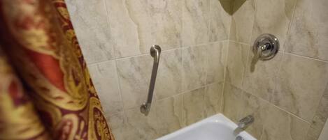 A bathroom with a white bathtub, a shower with a handheld showerhead, and a grab bar.
