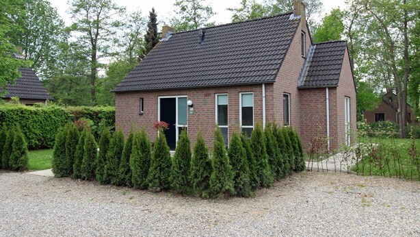 A brick house with a tiled roof, surrounded by a gravel driveway and neatly trimmed hedges. - Bright Bungalow in Peaceful Park Setting (Ewijk)