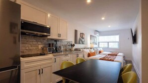 A modern kitchen with white cabinets, a black countertop, and a dining area with a black table and yellow chairs. - Charming Stay-3 min walk to metro (Montréal)