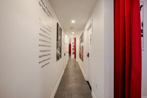 Um corredor com paredes brancas, cortinas vermelhas e quadros emoldurados.