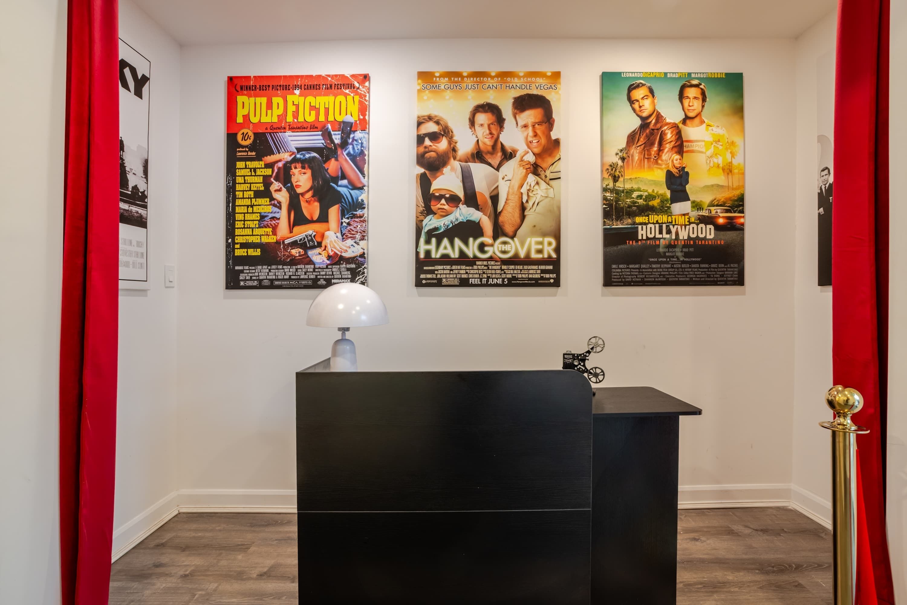 A room with a black desk, a lamp, and three movie posters on the wall.