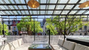 An outdoor seating area with a glass table, two sofas, and a view of the cityscape. - Ville-Marie Vibe – Modern Downtown Studio (Montréal)