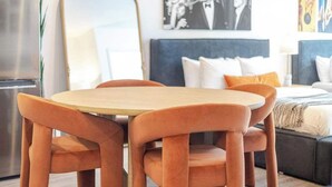A modern hotel room with a round wooden table and matching chairs, a bed with a dark headboard, and a large mirror on the wall. - The Zen Cityscape: Charming 1 BR Apt in DT MTL (Montréal)