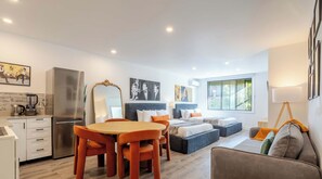 A modern hotel room with a dining area, a large bed, a sofa, and a view of the outdoors.