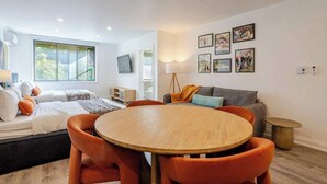 A modern bedroom with a bed, a round wooden table, orange chairs, a grey sofa, and a TV on the wall. - The Zen Cityscape: Charming 1 BR Apt in DT MTL (Montréal)