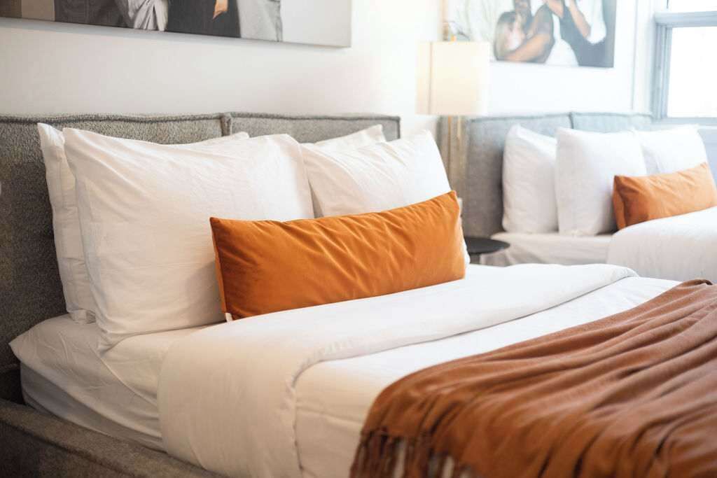 A hotel room with a bed, white bedding, and a brown throw blanket.