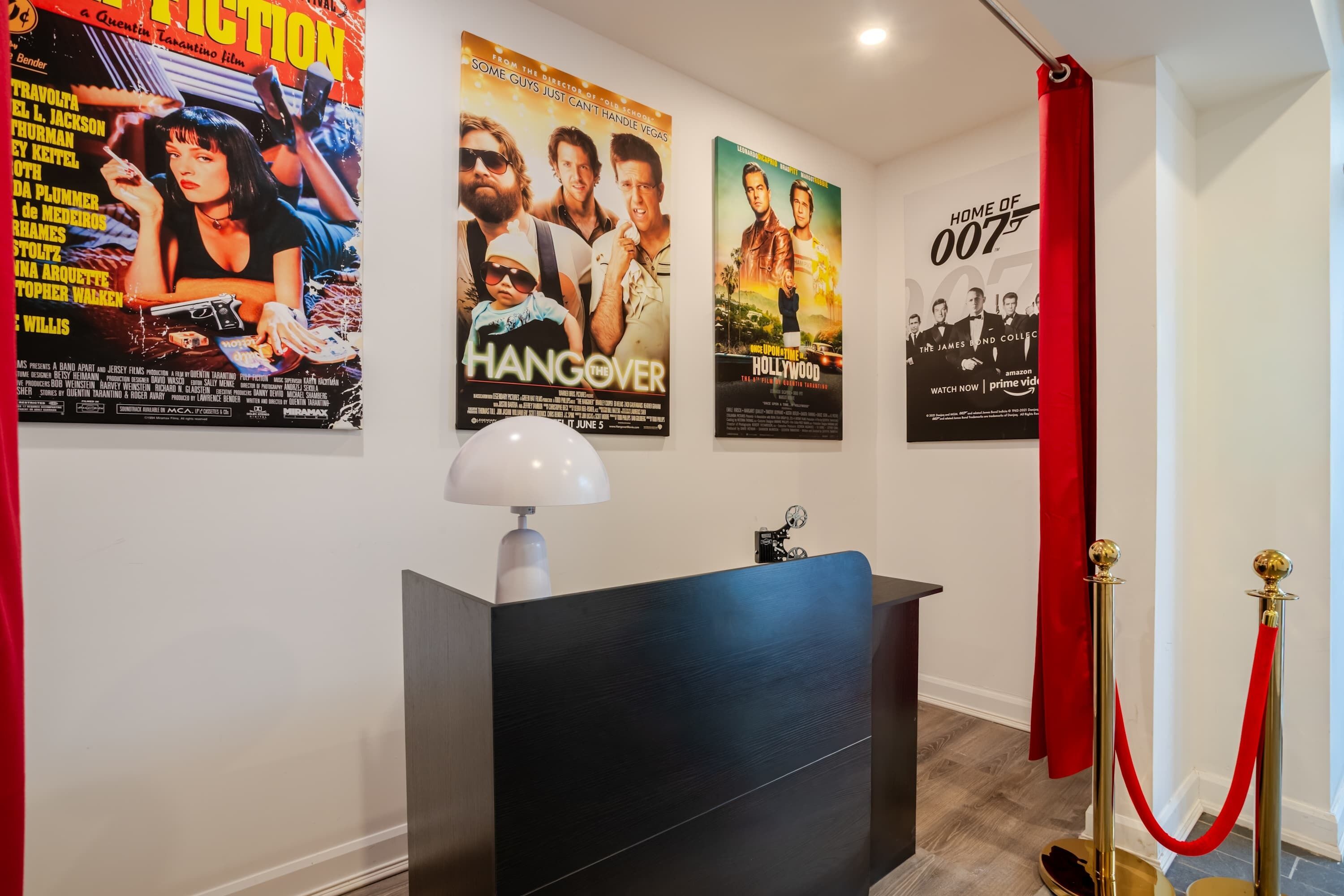 A hotel lobby with a reception desk, red velvet ropes, and movie posters on the wall.