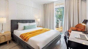 A modern hotel room with a large bed, a desk with a laptop, and a view of the outdoors.