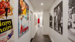 A corridor with posters on the walls, a door at the end, and a red door in the background.