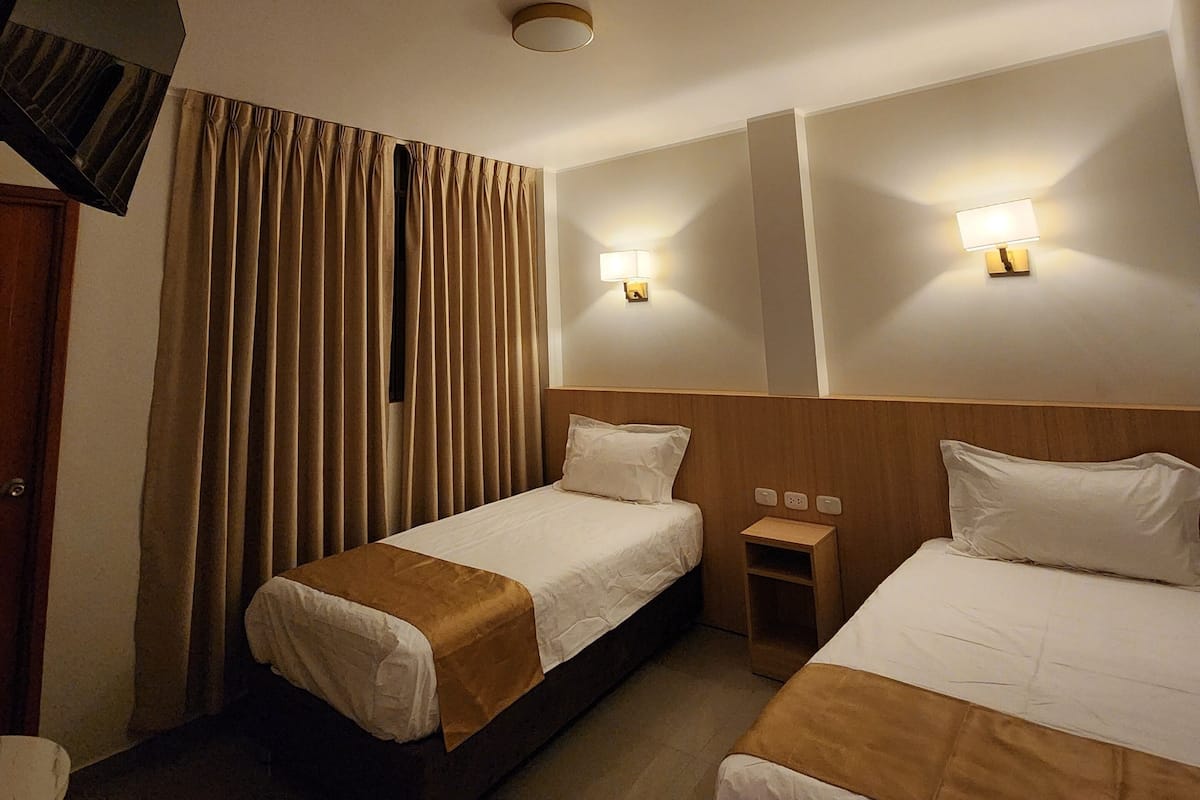 Habitación de hotel con dos camas, televisión, una mesita y una lámpara de pared.