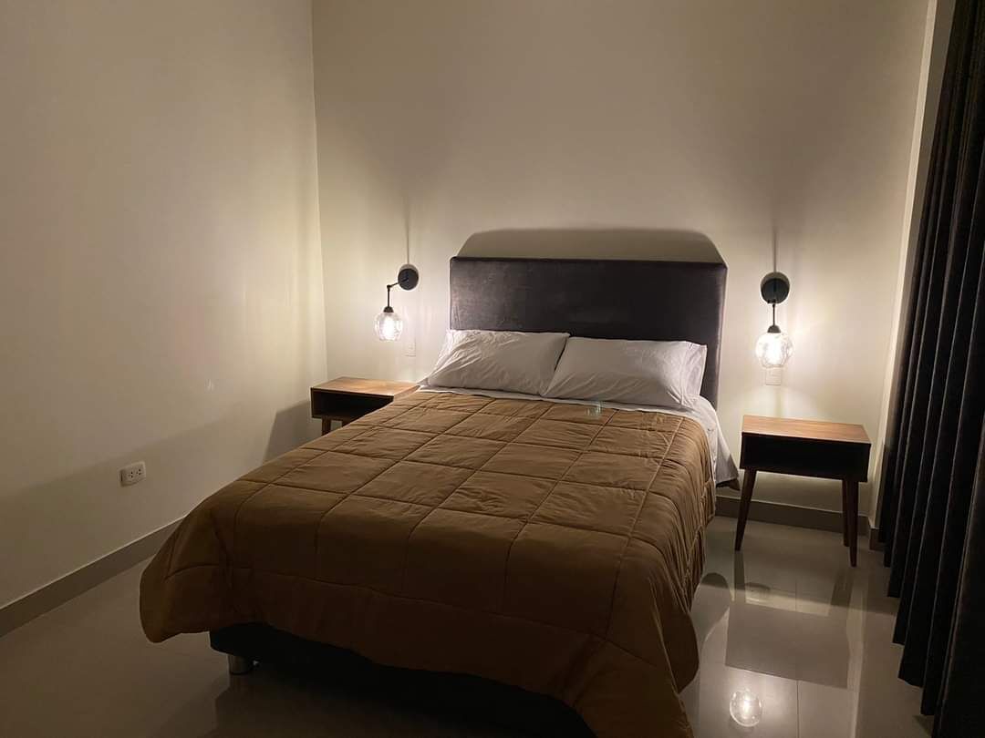 Un dormitorio con una cama, dos mesitas de noche y dos lámparas de pared.