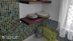 A kitchen with tiled backsplash, wooden shelves, and a window with sheer curtains.