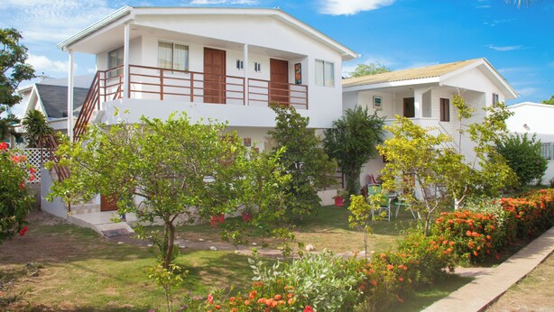 A two-story white building with a balcony, surrounded by a well-maintained garden with various plants and flowers.