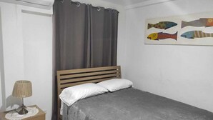 A bedroom with a bed, a lamp, a curtain, and a fish painting on the wall.
