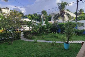 Un jardín residencial con un camino, palmeras y un coche blanco estacionado al fondo.