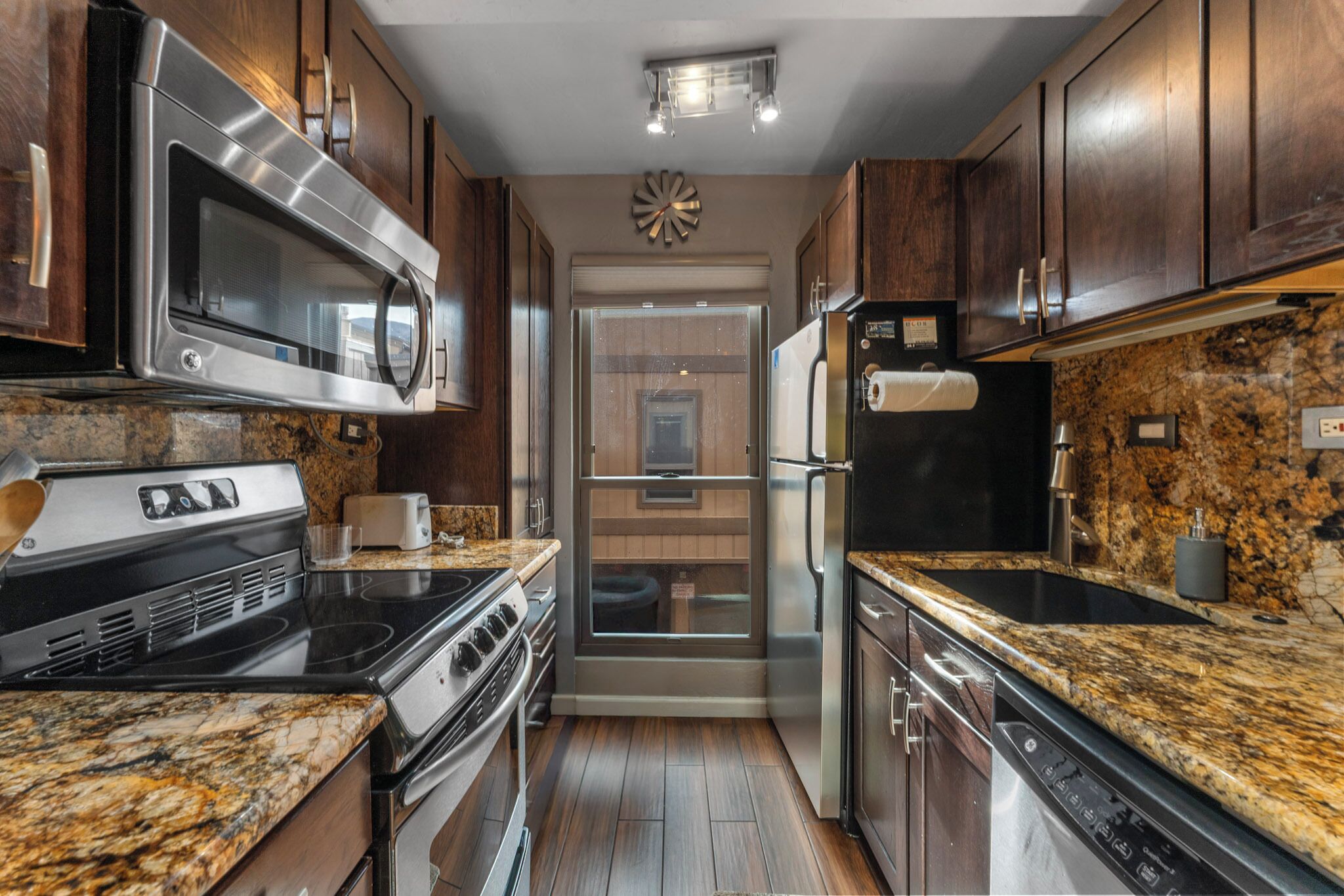 A modern kitchen with stainless steel appliances, wooden cabinets, granite countertops, and a built-in oven.