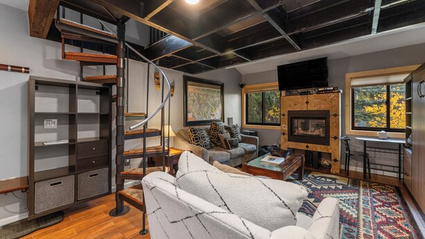 A modern living room with a fireplace, a sofa, a coffee table, and a staircase with a metal railing. - Rc5b0 (Breckenridge)